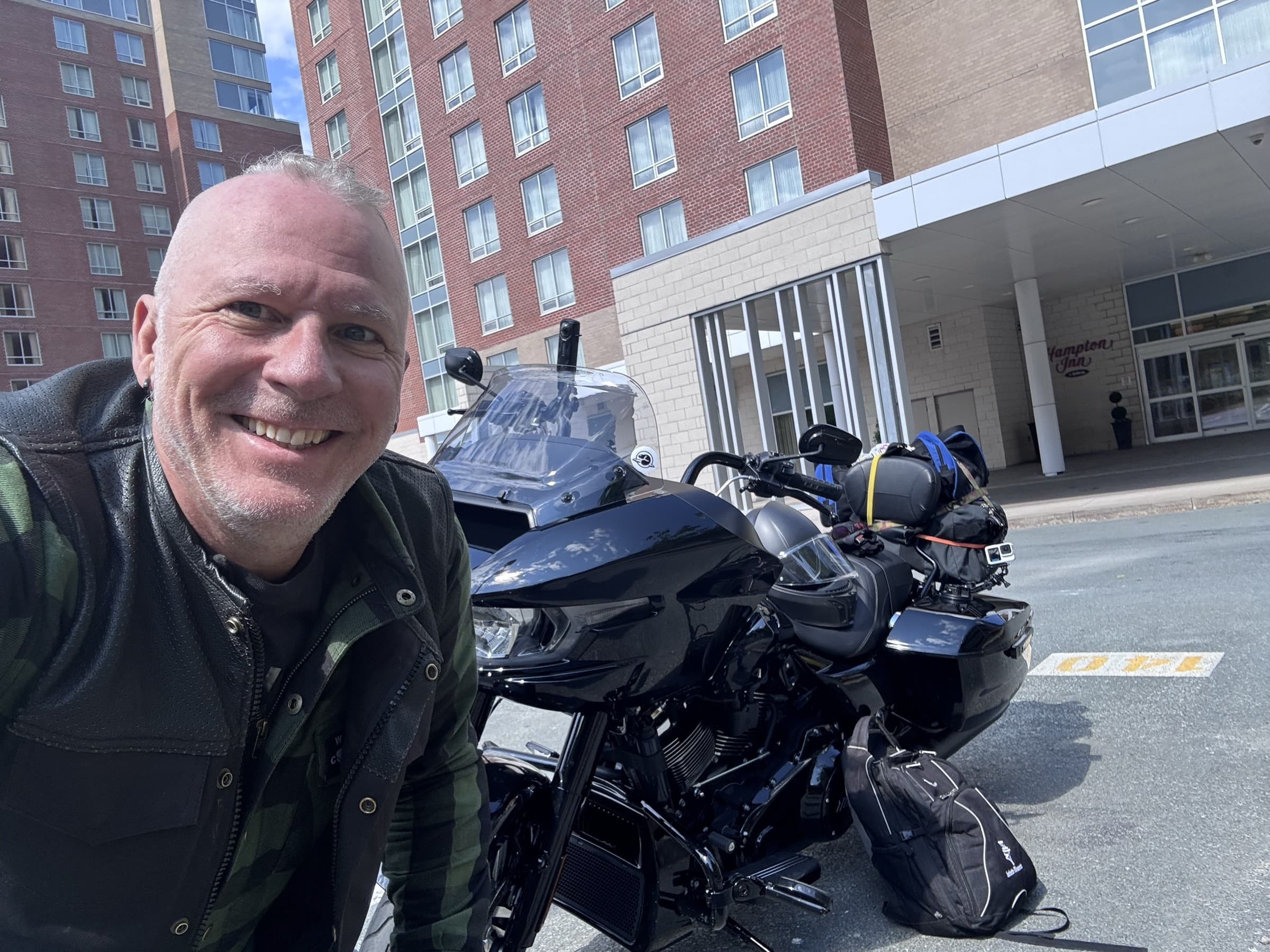 Michael Dargie smiling beside a touring motorcycle outside a hotel on the East Coast Book Tour