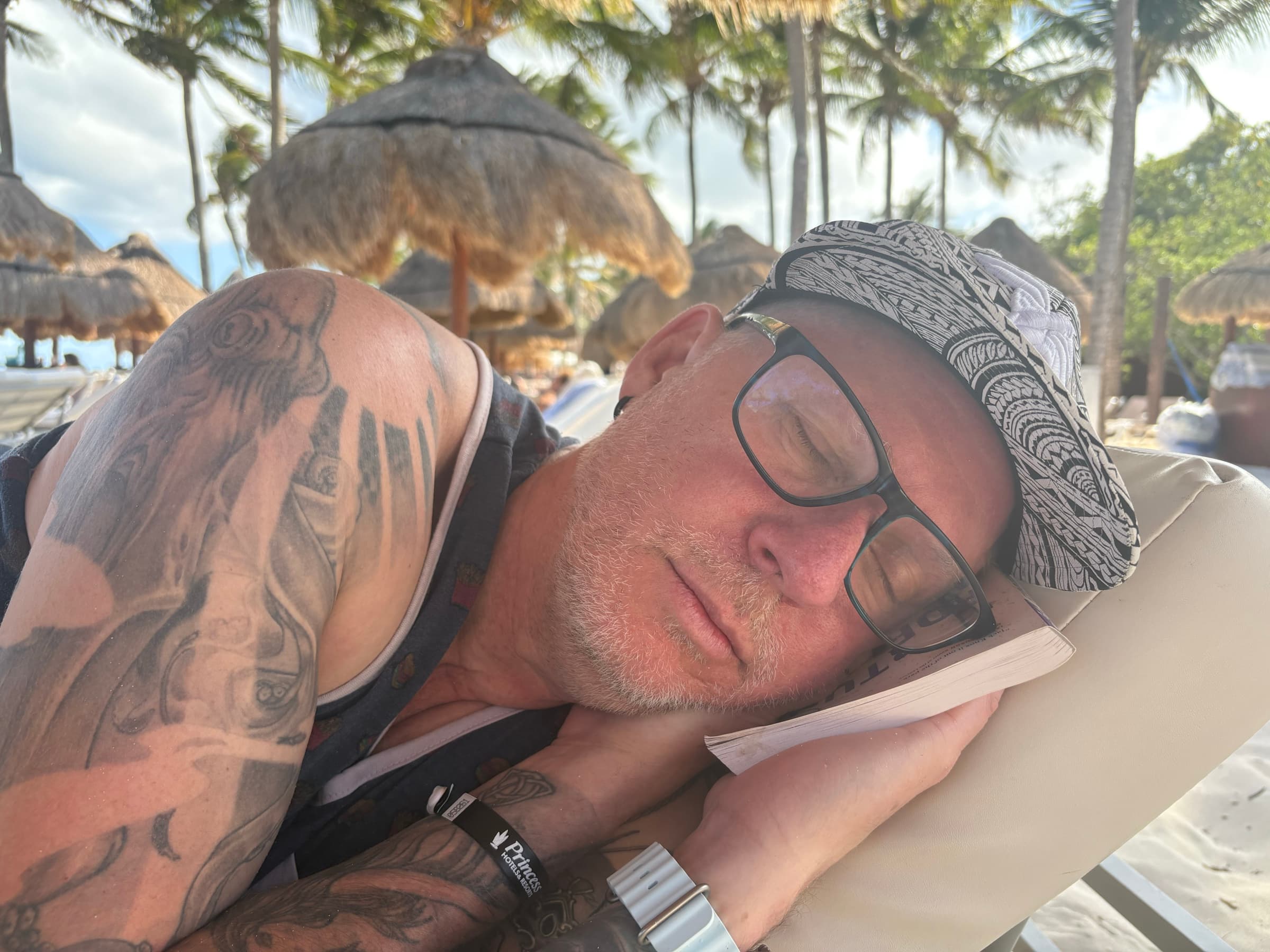 Michael Dargie reading on a beach lounger under palm thatch