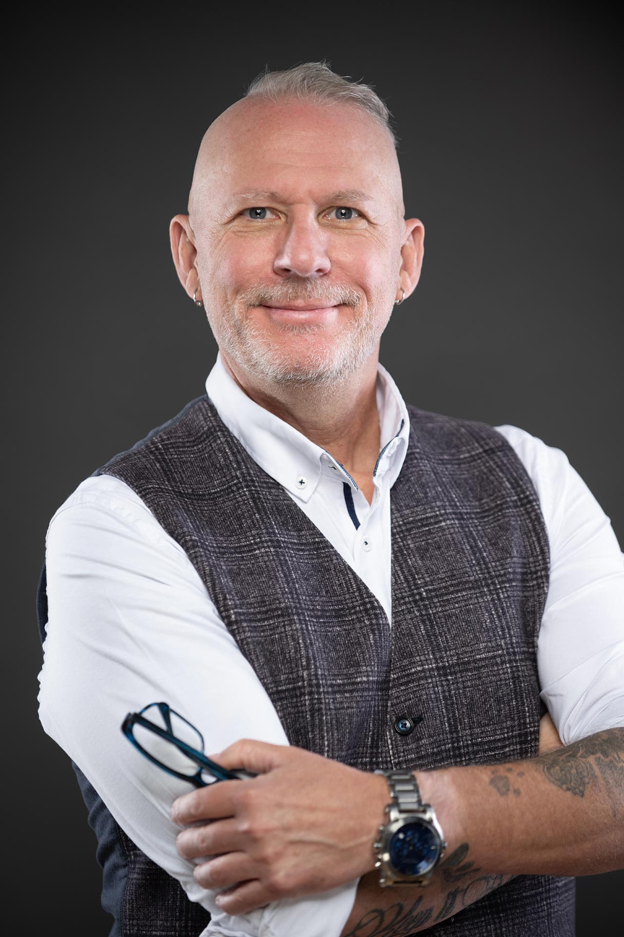 Michael Dargie in a grey vest and white shirt, glasses held in hand, editorial pose