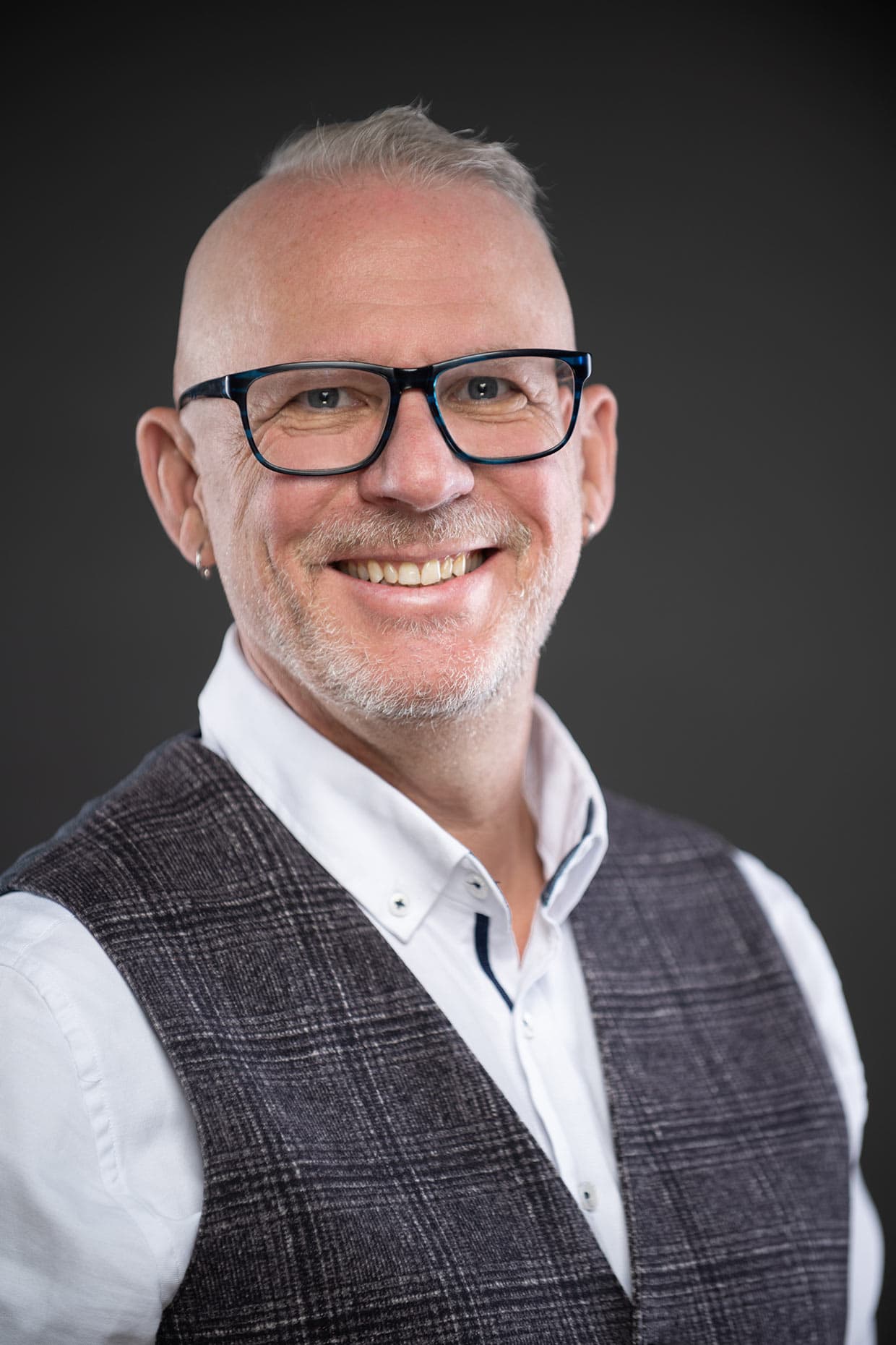 Michael Dargie in a grey vest and white shirt, smiling, glasses on