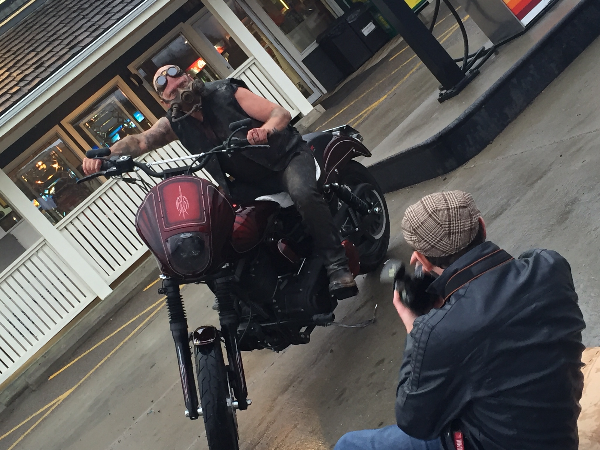 Michael Dargie in goggles and a gas mask on a custom motorcycle while a photographer shoots from below