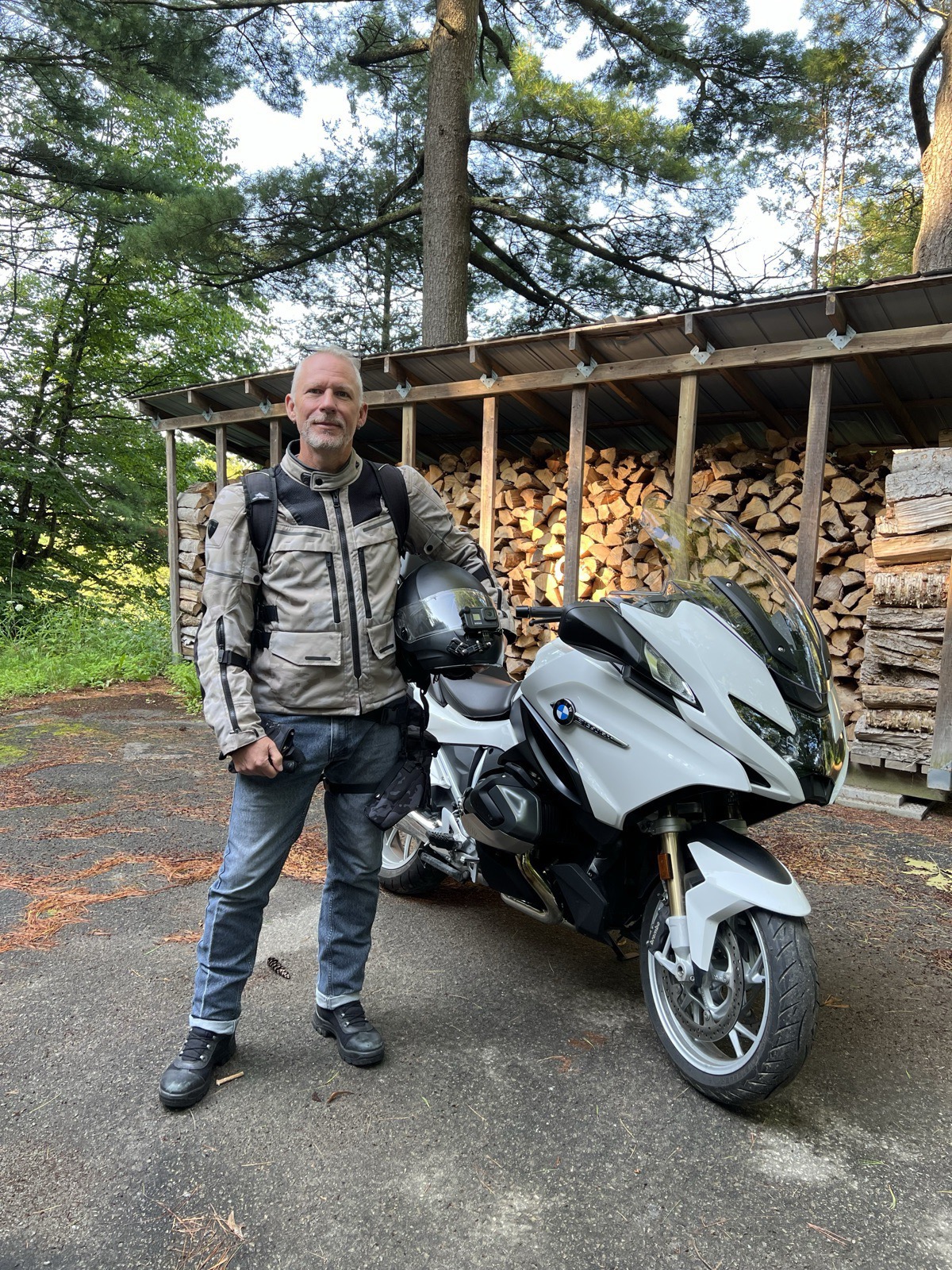Michael Dargie in riding gear beside a white BMW touring motorcycle in front of a woodshed